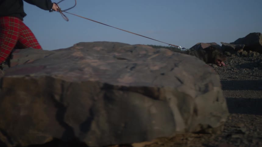 Woman carries her jacket as she walks her dog among mountain rocks