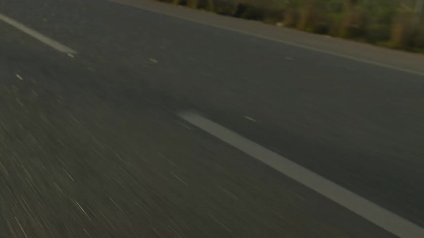 A lowangle view captures a stretch of asphalt road rushing past its white lane marking cutting diagonally through the frame as motion blur and warm light suggest speed travel and forward momentum