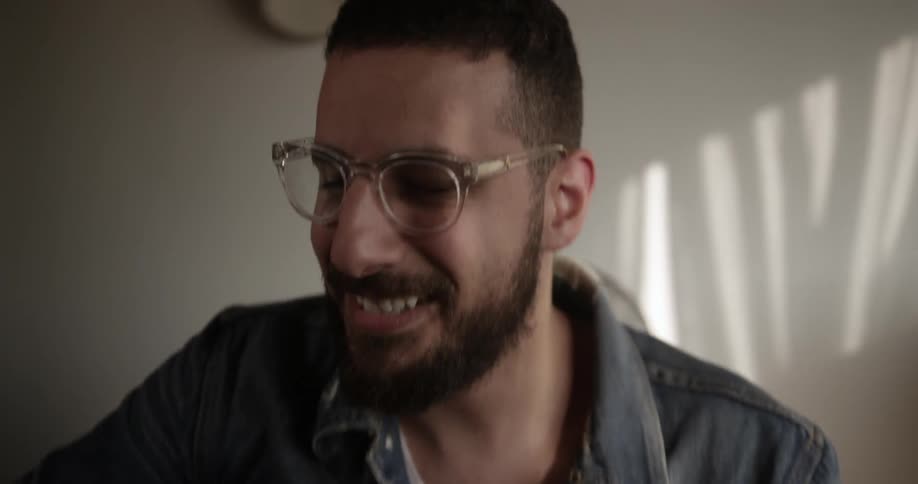 A man laughs while playing an acoustic guitar