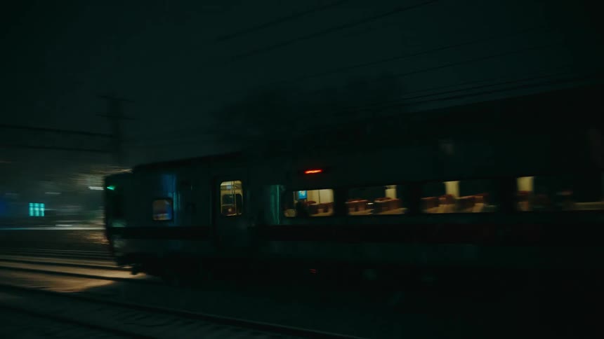 Train moves along the tracks at night during heavy rain with headlights illuminating the railway