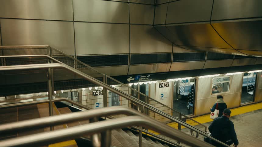 People carry their belongings as they walk down the stairs in the subway as a train is waiting for passengers