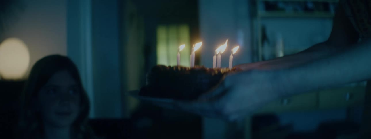 A mother carrying a cake with lit candles bringing it to her daughter at the dining table to celebrate her birthday indoors