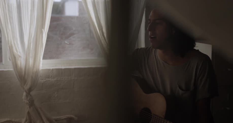 A man is playing the guitar by the window