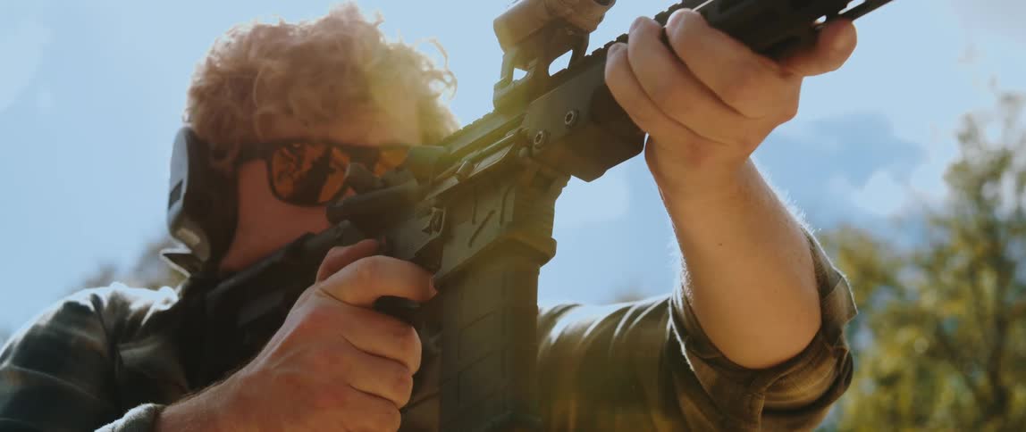 Man firing a rifle in an open field