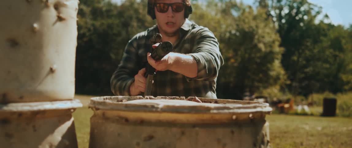 Man runs carrying his rifle and leans over a barrel looking through the scope