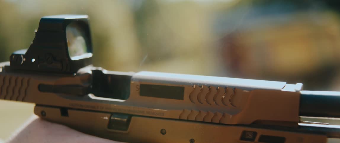 A handgun is fired in slow motion showing a shell casing being ejected as smoke rises from the open chamber the firearm is equipped with a red dot sight and a tactical light with the slide locking back after the final shot
