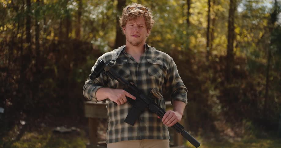 A man stands holding a rifle