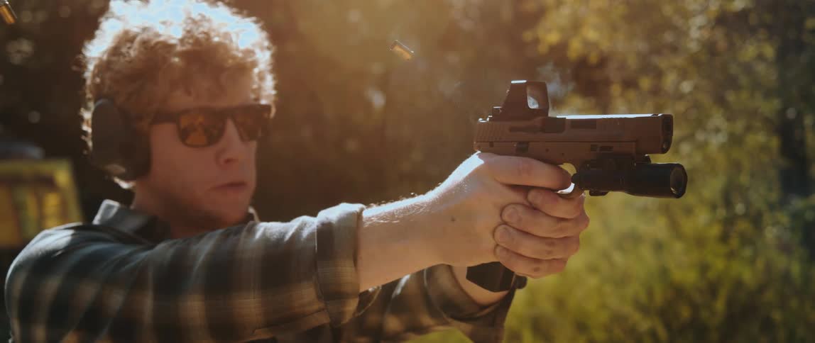 In this video a man wearing sunglasses and ear protection repeatedly fires a handgun equipped with a red dot sight and a flashlight spent shell casings are seen ejecting into the air as he maintains a steady grip on the firearm outdoors