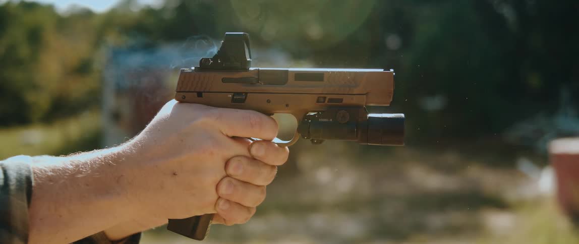Man holds a pistol with both hands and fires shots as bullet shells fly into the air