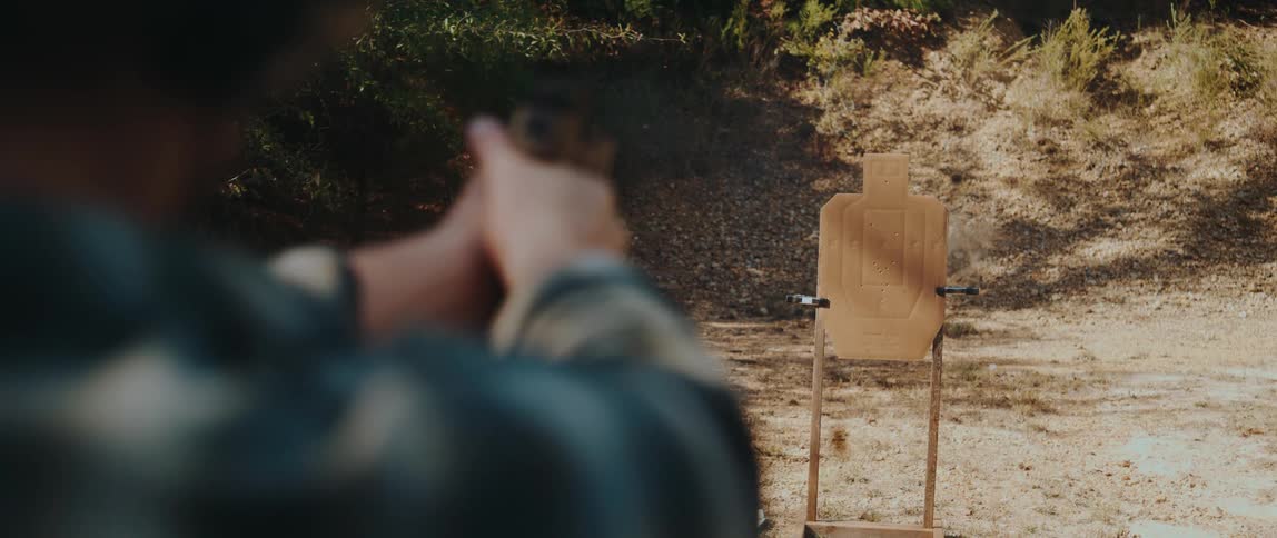 Person shooting at a paper target mounted on a wooden stand in an outdoor shooting range