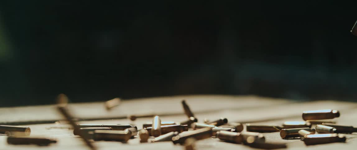 Spent bullet casings scatter and bounce as they strike a wooden surface