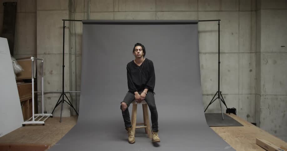 A man walks into a studio and sits on a stool