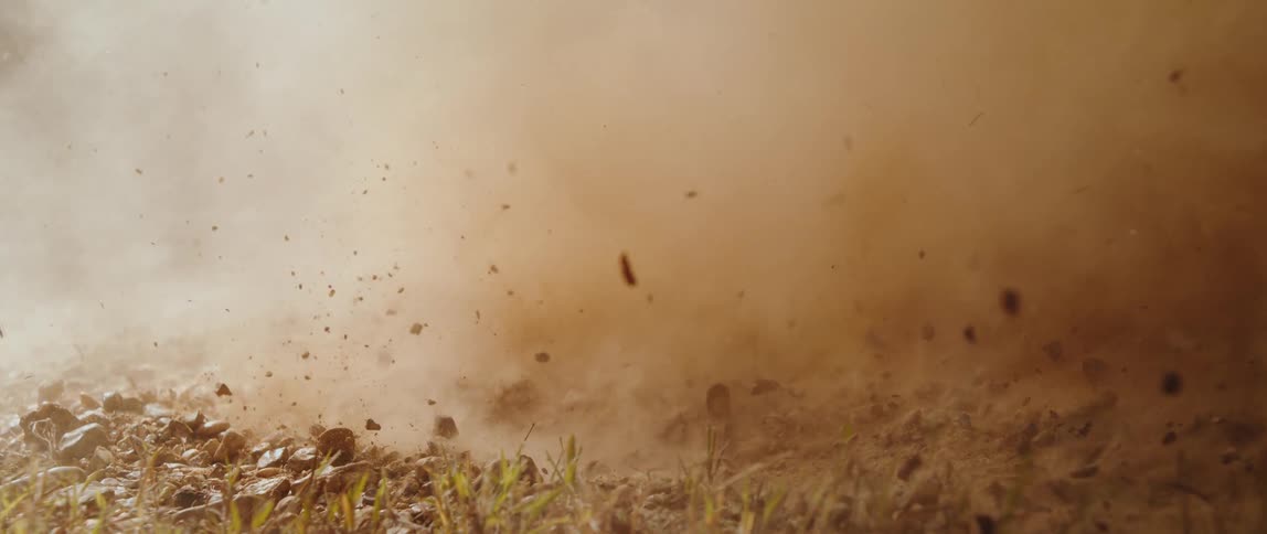 In a dramatic slowmotion blast dirt and small rocks erupt from the ground filling the air with a thick swirling cloud of dust
