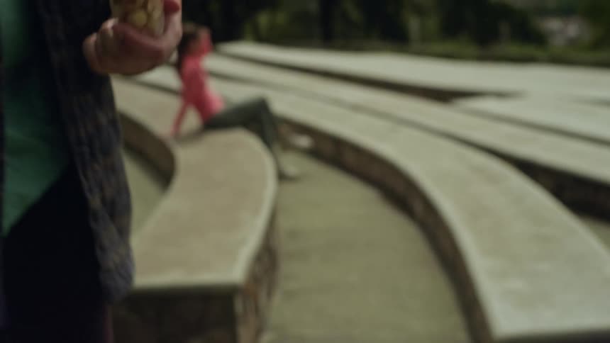 A close view shows a mans hand holding a small plastic cup filled with fruit and nut snacks near stone park benches