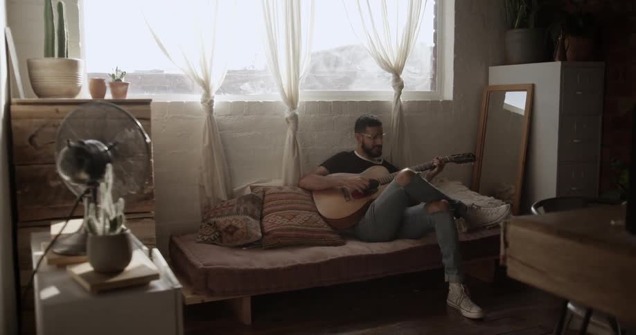 A man sits on a sofa playing the guitar