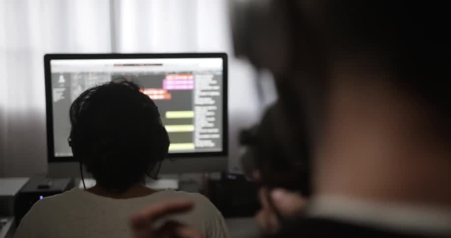 Person talks into a microphone while another looks at a monitor