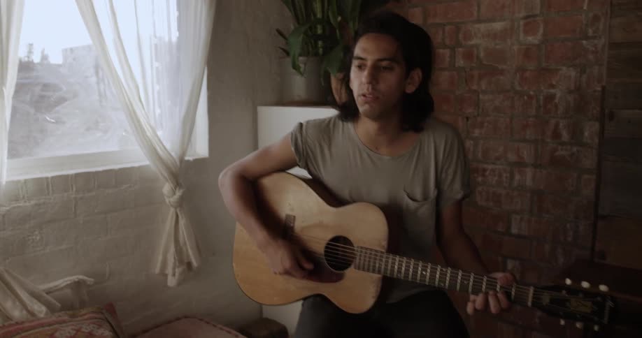 A man plays guitar near the brick wall