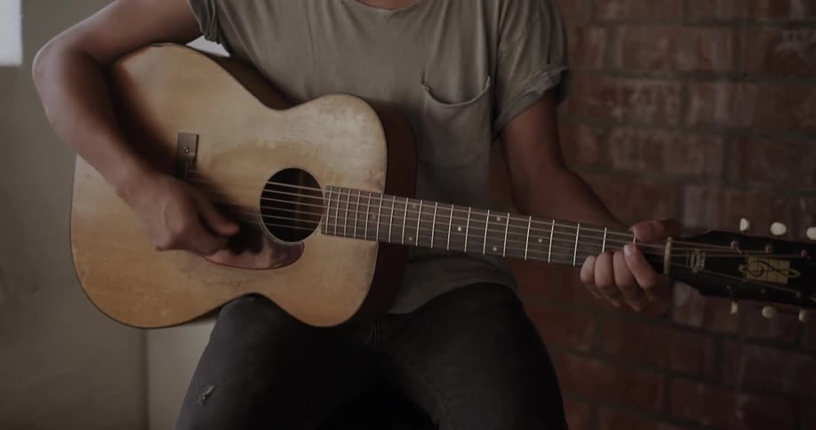 A man sits on a stool playing guitar