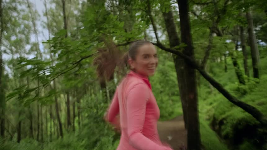 Young woman runs into the woods turning and motioning to the person behind her