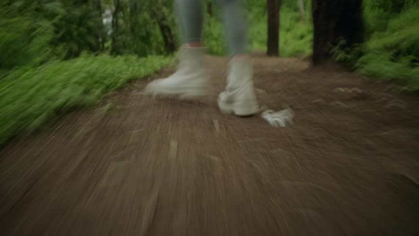 A person in white boots runs quickly down a dirt path through a lush forest