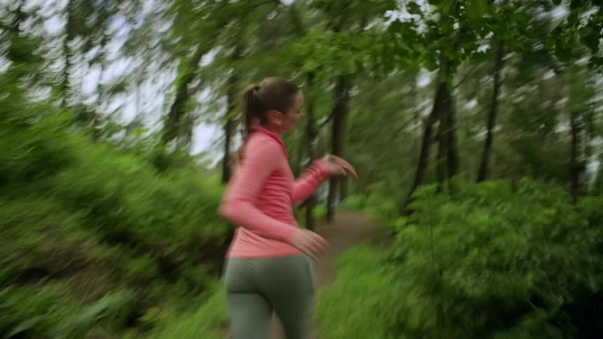 A woman joyfully jogs along a forest trail surrounded by lush green trees