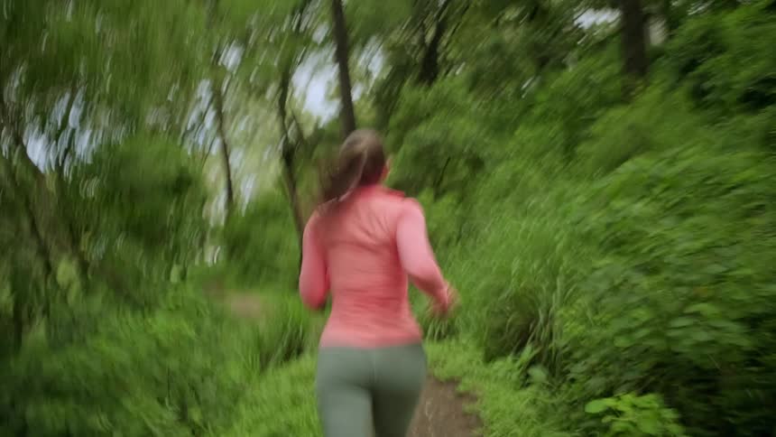 The woman turns back while running on a forest trail