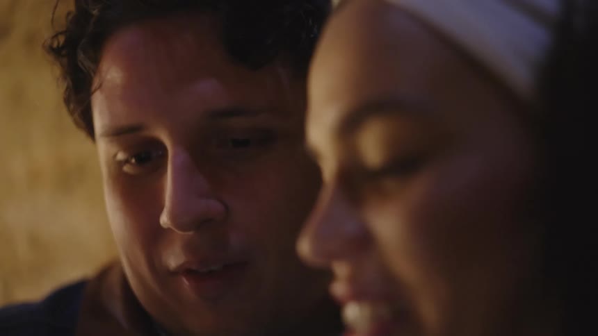 In this closeup video a man and a woman are shown smiling and talking to each other in a dimly lit setting the woman wears a white headband and both appear to be engaged in a happy casual conversation