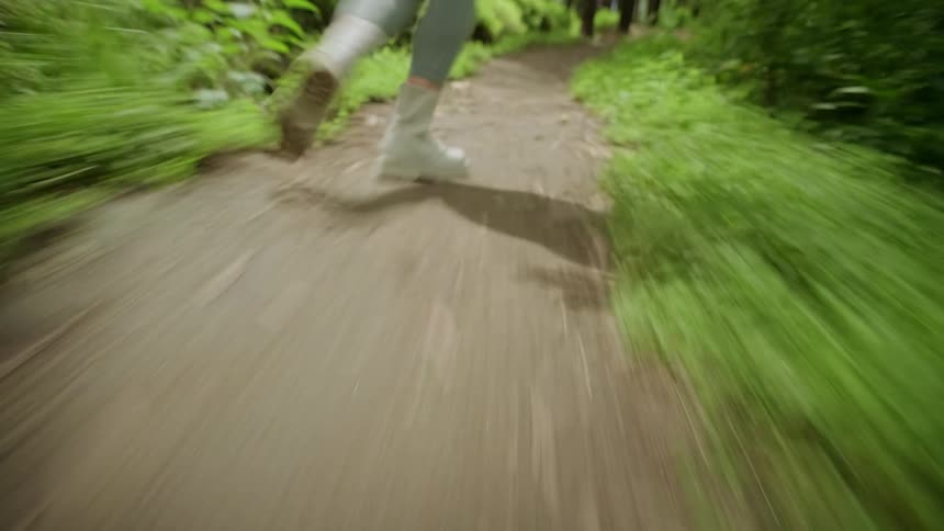 A person runs quickly down a narrow forest path surrounded by blurred greenery