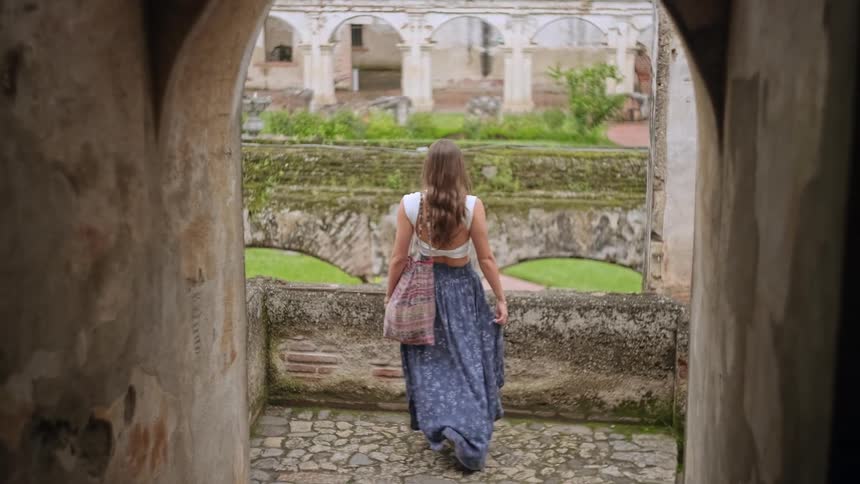 Woman looks out over a historic courtyard from a stone arch in architectural ruins