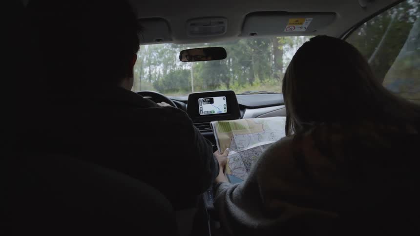 Passenger pointing directions while holding a map with the driver navigating a road surrounded by trees