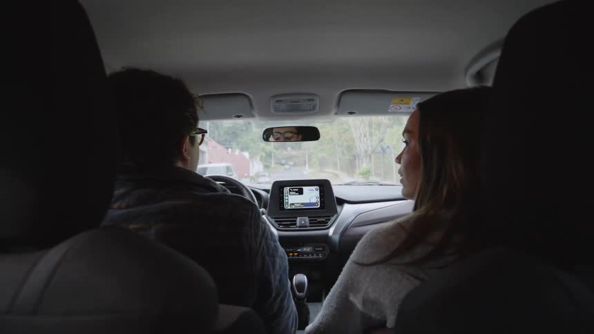 A couple seated inside a car at midday driving while having a conversation