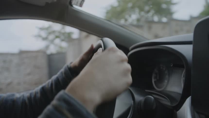 Closeup of a hand gripping a steering wheel while driving through a neighborhood