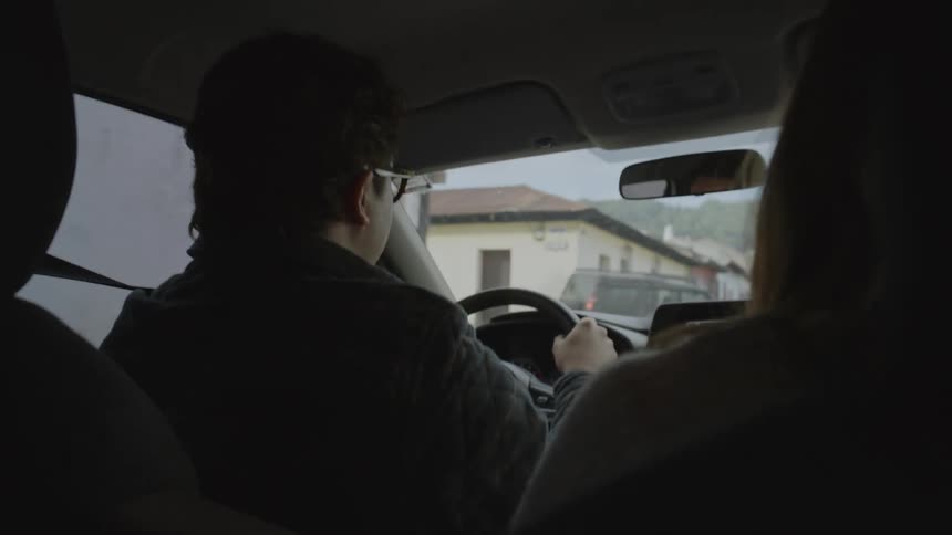 A couple rides in a car as the man drives through a quiet suburban neighborhood during the day