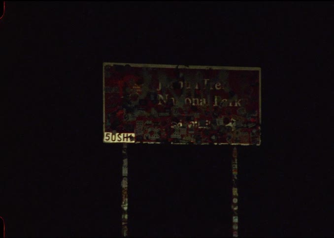 Road sign for Joshua Tree that is vandalized with graffiti on a highway at night