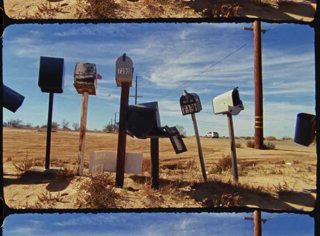 A row of mailboxes on the side of a desert road with cars driving by on a sunny day