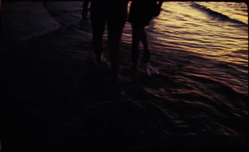 A couple walking side by side on the beach at sundown with waves washing over their feet