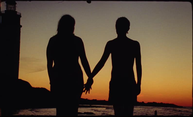 Silhouette of two people holding hands facing the sea