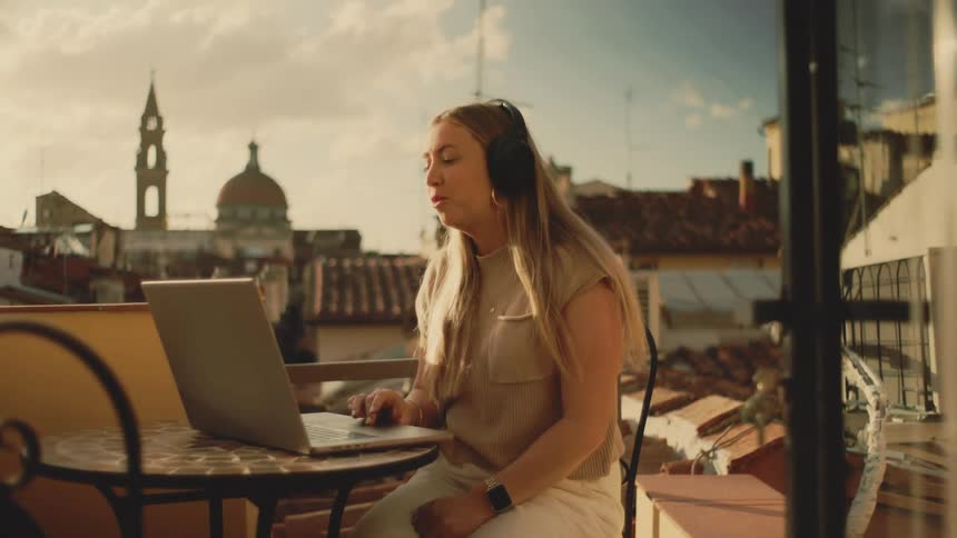 The woman is talking on her laptop while on the balcony