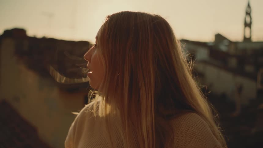 Woman looks over the city at sunset with wind moving her hair