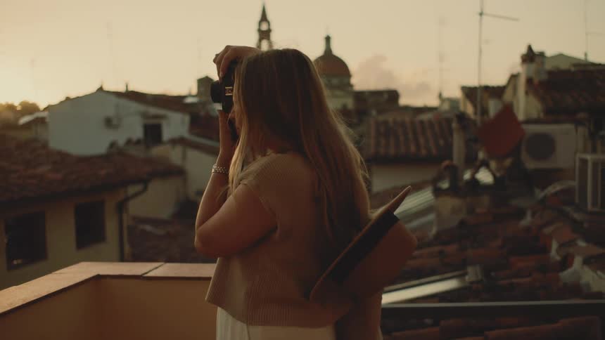 The woman takes photos on the balcony at sunrise