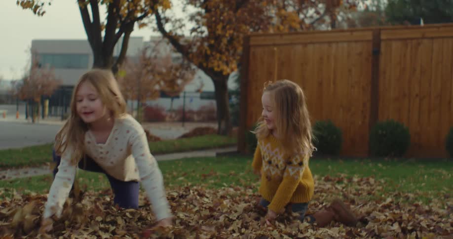 Two young girls playing in the front yard and throwing leaves into the air