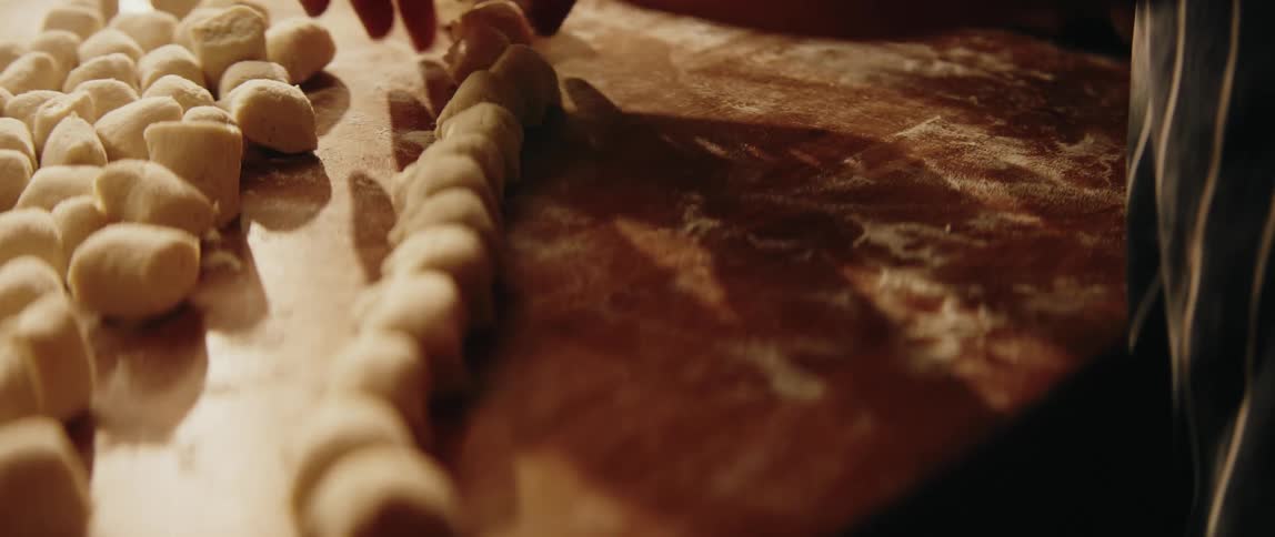 Hands shaping small pieces of dough arranged on a floured surface