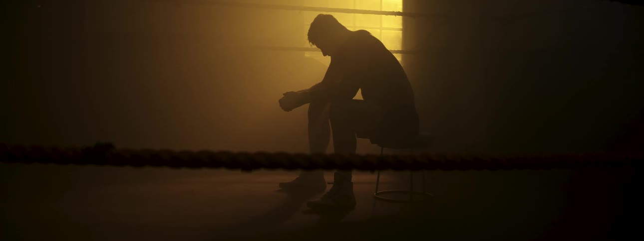 Boxer sitting on a stool inside the ring in silhouette with visible ropes and low backlighting