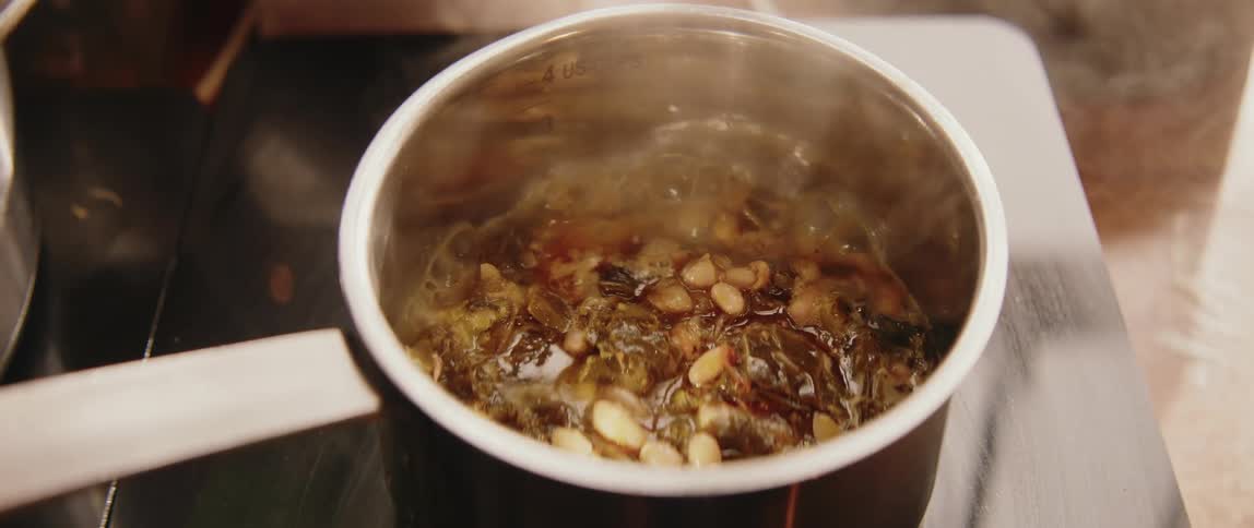 A metal pot filled with beans and green leafy vegetables simmers on a black stovetop with steam rising from the boiling water