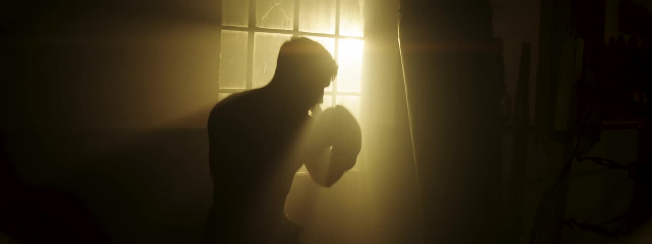Boxer striking a training bag in silhouette in front of a backlit window indoors