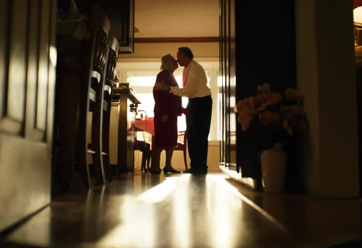 Elderly couple standing in the hallway as he gives her a kiss