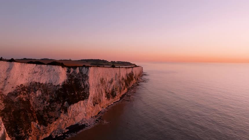 Coastal cliffs lit by the sunset with white rock faces above calm seawater