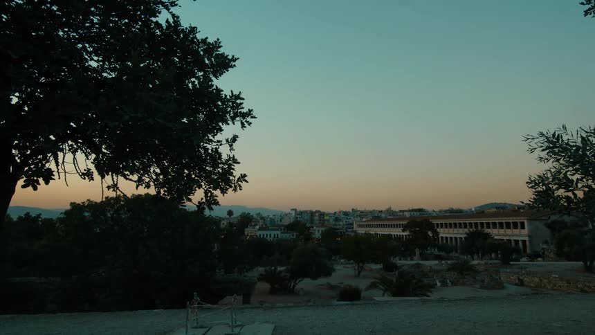 Red tints the sky over the hills bordering a town in the summer