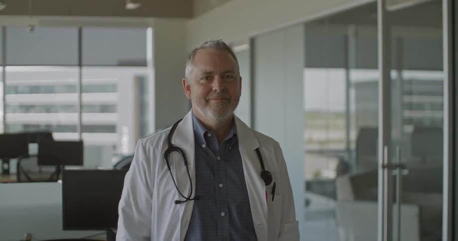 Video Portrait of Doctor in a modern clinical environment wearing a lab coat and stethoscope with glass walled rooms in the background