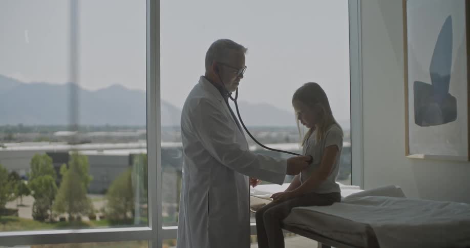 Male doctor uses his stethoscope during the checkup of a young girl